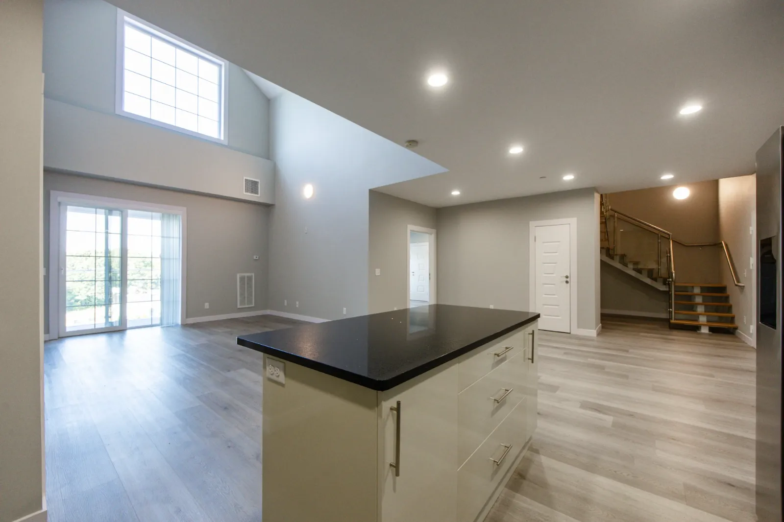 Open-plan kitchen and living area with a double-height window and loft stairs